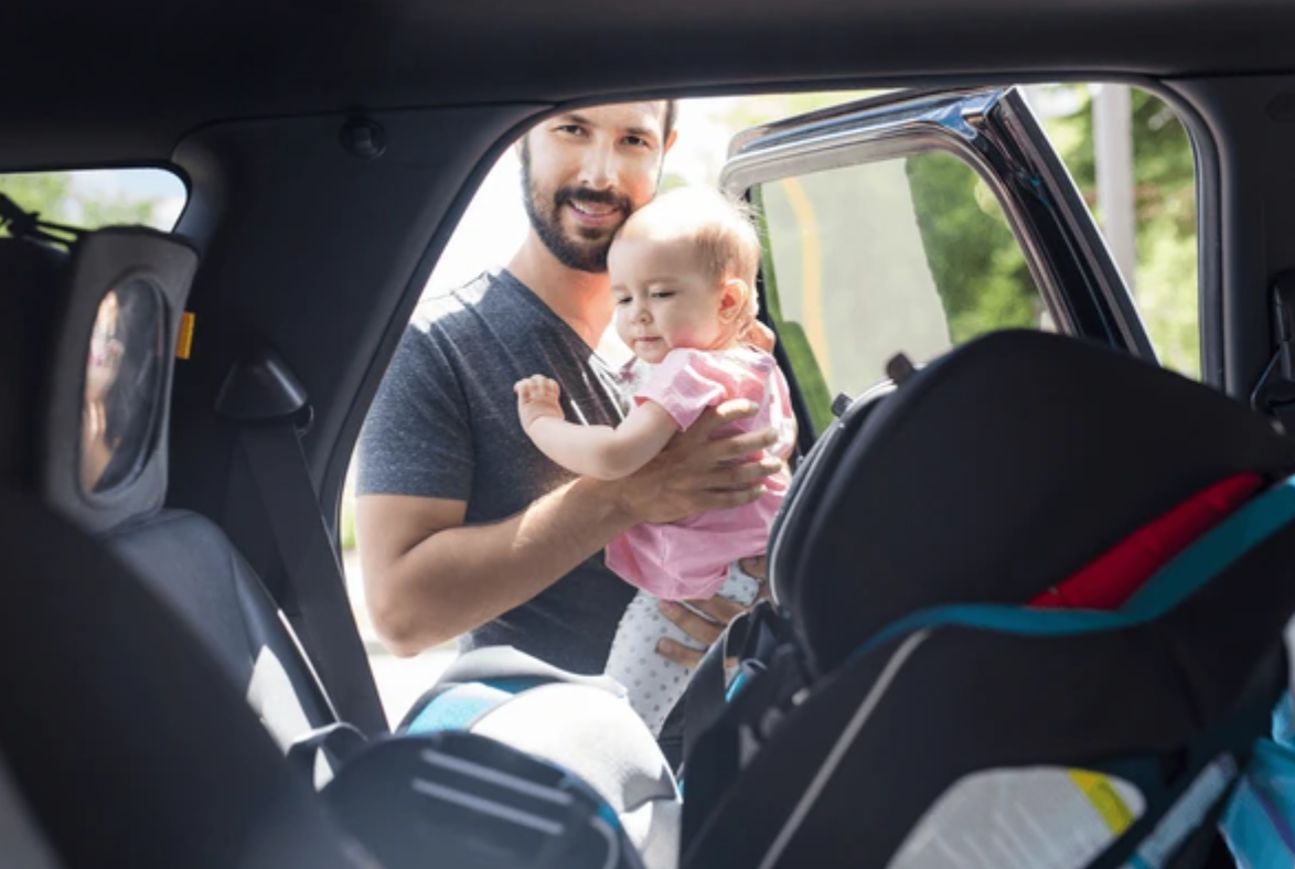 Father placing baby into a rear-facing car seat during consultation